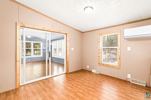 empty room featuring visible vents, wood finished floors, vaulted ceiling, an AC wall unit, and a wealth of natural light