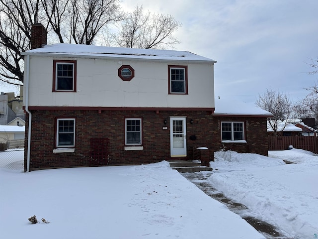 colonial house featuring brick siding, a chimney, and fence