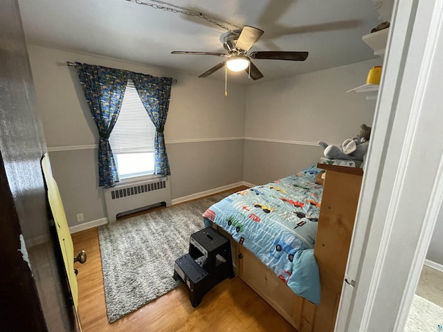 bedroom featuring baseboards, wood finished floors, a ceiling fan, and radiator