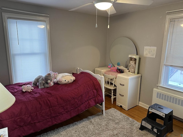 bedroom featuring baseboards, ceiling fan, radiator heating unit, and wood finished floors