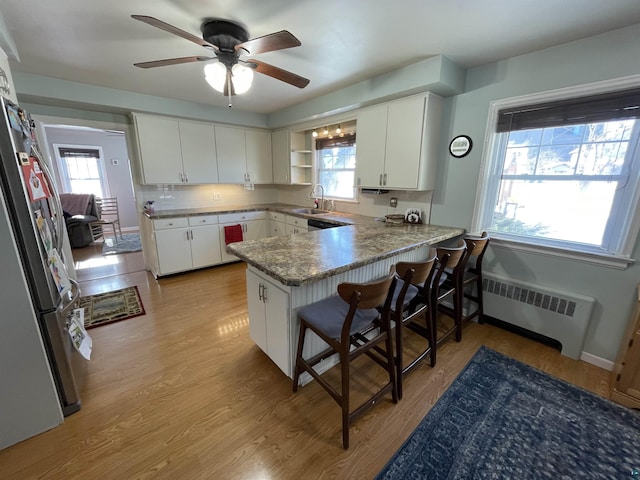 kitchen featuring light wood finished floors, radiator heating unit, freestanding refrigerator, a peninsula, and a sink