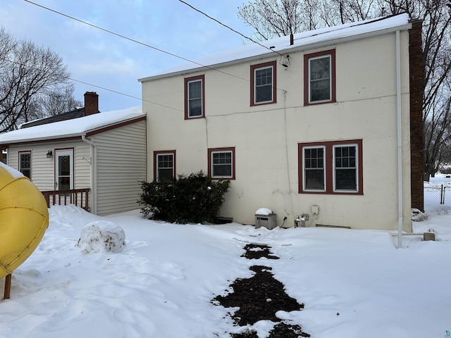 snow covered house with fence, a chimney, and stucco siding