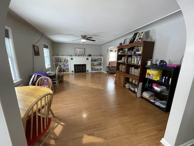 interior space with arched walkways, wood finished floors, a ceiling fan, baseboards, and a brick fireplace