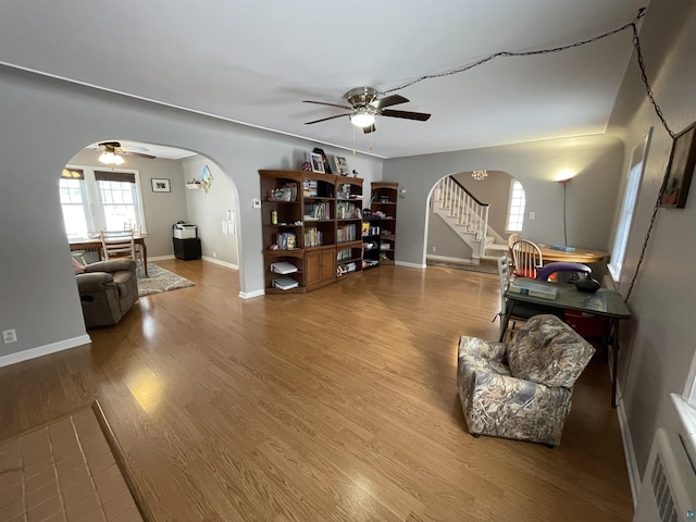 sitting room featuring ceiling fan, stairs, arched walkways, and wood finished floors