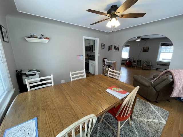 dining space with radiator, a ceiling fan, arched walkways, and wood finished floors