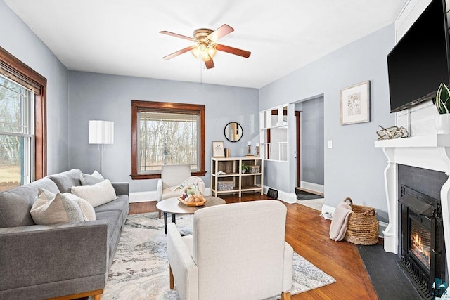 living room with a fireplace with flush hearth, ceiling fan, baseboards, and wood finished floors