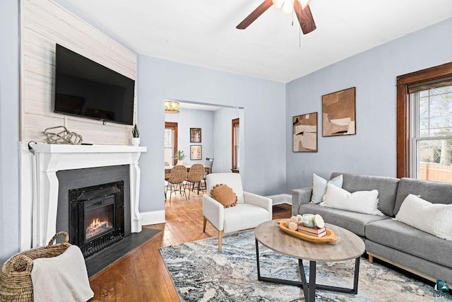 living area featuring ceiling fan, hardwood / wood-style floors, a fireplace with flush hearth, and baseboards