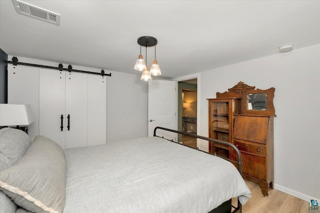 bedroom featuring light wood-type flooring, a barn door, visible vents, and baseboards