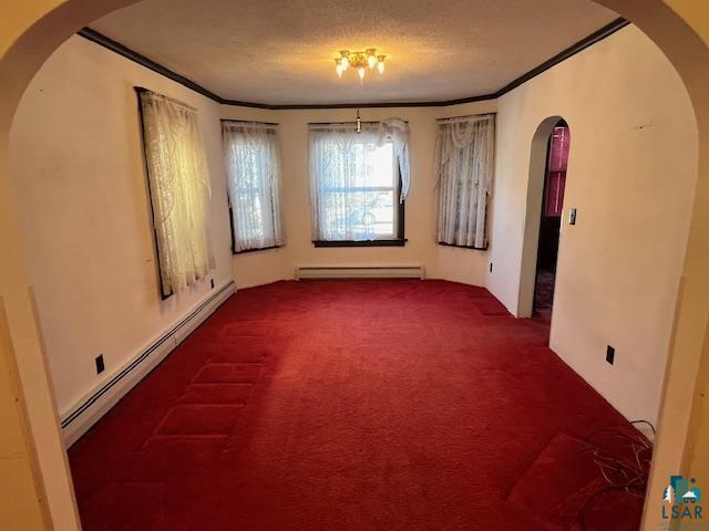 carpeted spare room with a baseboard heating unit, crown molding, arched walkways, and a textured ceiling