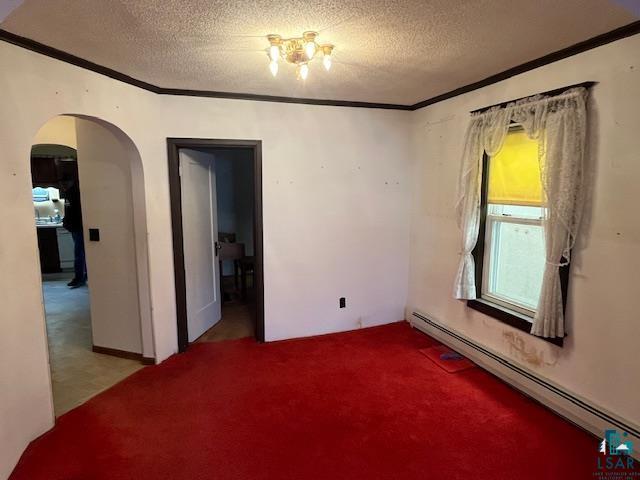 spare room with arched walkways, a textured ceiling, baseboard heating, carpet, and crown molding