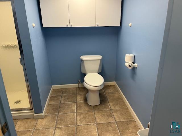 full bath featuring tile patterned flooring, a shower stall, toilet, and baseboards