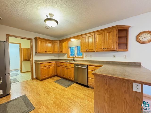 kitchen featuring brown cabinetry, light wood-style flooring, appliances with stainless steel finishes, a peninsula, and a sink