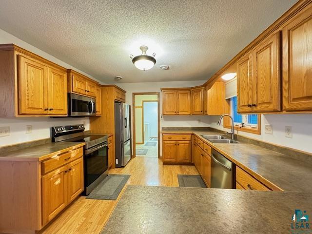 kitchen featuring light wood finished floors, appliances with stainless steel finishes, brown cabinets, a textured ceiling, and a sink