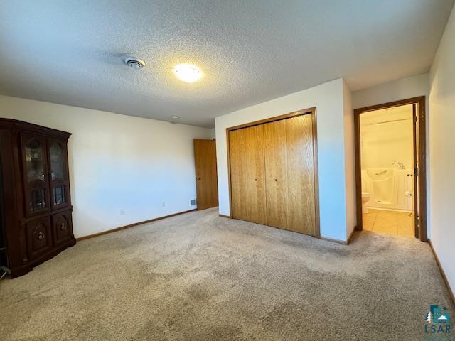 unfurnished bedroom featuring light carpet, a textured ceiling, baseboards, and a closet