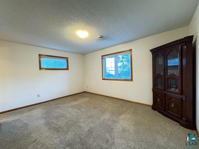 carpeted empty room featuring baseboards and a textured ceiling