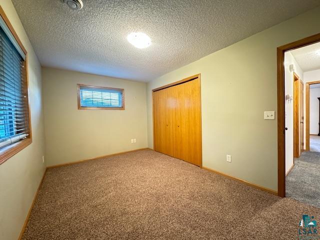 unfurnished bedroom with a textured ceiling, a closet, carpet, and baseboards