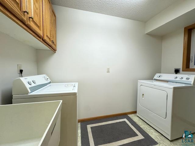 laundry room featuring a textured ceiling, separate washer and dryer, cabinet space, and baseboards