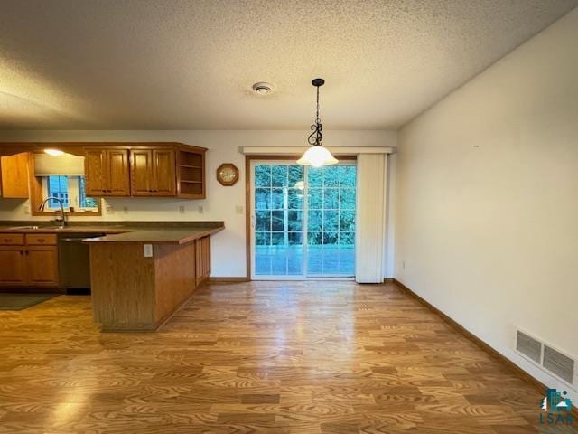 kitchen with visible vents, brown cabinets, wood finished floors, a peninsula, and stainless steel dishwasher