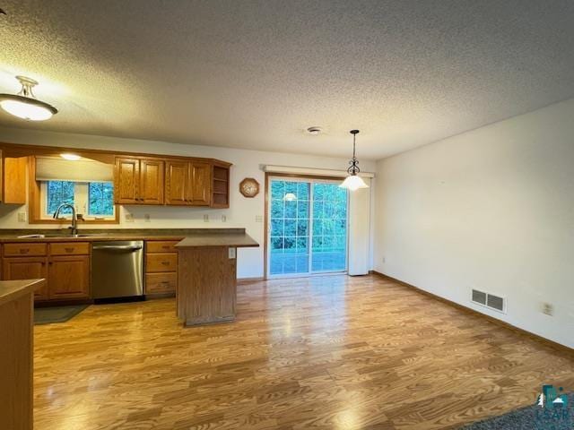 kitchen featuring visible vents, brown cabinetry, stainless steel dishwasher, light wood-style floors, and a sink