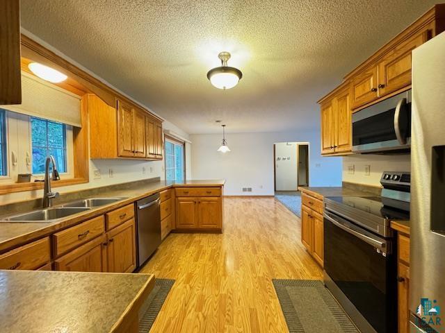 kitchen featuring appliances with stainless steel finishes, brown cabinetry, a sink, light wood-type flooring, and a peninsula