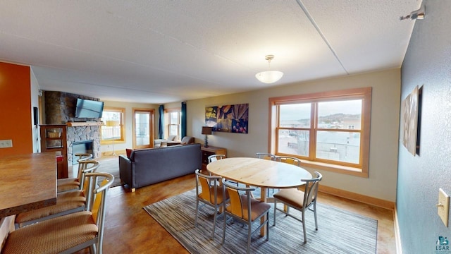 dining space featuring a healthy amount of sunlight, baseboards, a textured ceiling, and a stone fireplace