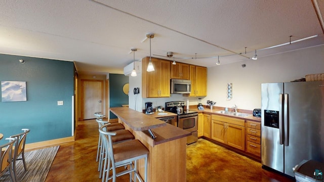 kitchen featuring a textured ceiling, stainless steel appliances, a peninsula, a sink, and finished concrete flooring