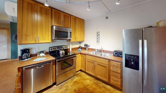 kitchen featuring concrete flooring, a sink, light countertops, appliances with stainless steel finishes, and brown cabinetry