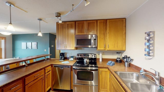 kitchen featuring decorative light fixtures, stainless steel appliances, brown cabinetry, a sink, and a peninsula