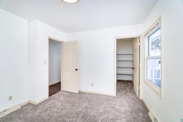 unfurnished bedroom featuring carpet floors, a walk in closet, visible vents, and baseboards