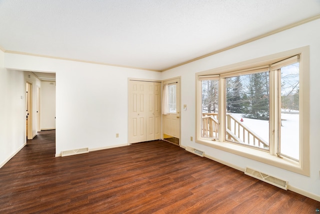 empty room featuring dark wood-style floors, visible vents, and ornamental molding