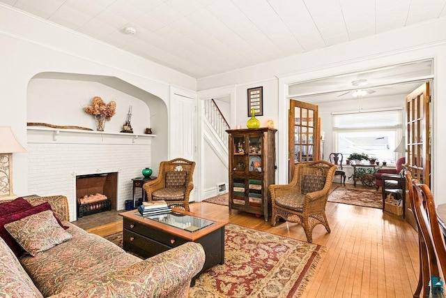 living room with ornamental molding, a brick fireplace, wood-type flooring, and stairs