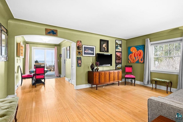 living room with arched walkways, light wood-style flooring, and baseboards