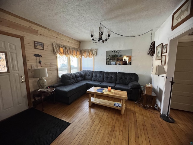 living area featuring a textured ceiling, wooden walls, hardwood / wood-style floors, and an inviting chandelier