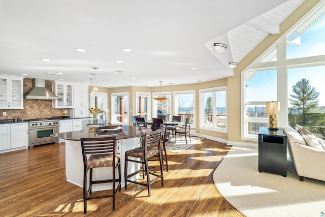 kitchen with white cabinetry, wall chimney range hood, high end stainless steel range oven, tasteful backsplash, and a kitchen bar