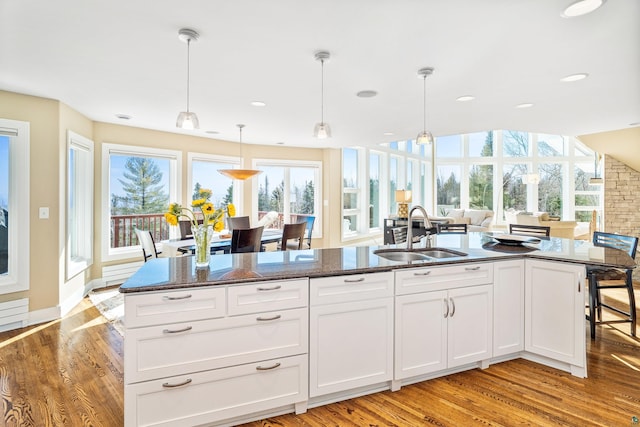 kitchen featuring a sink, white cabinetry, light wood finished floors, dark stone countertops, and pendant lighting