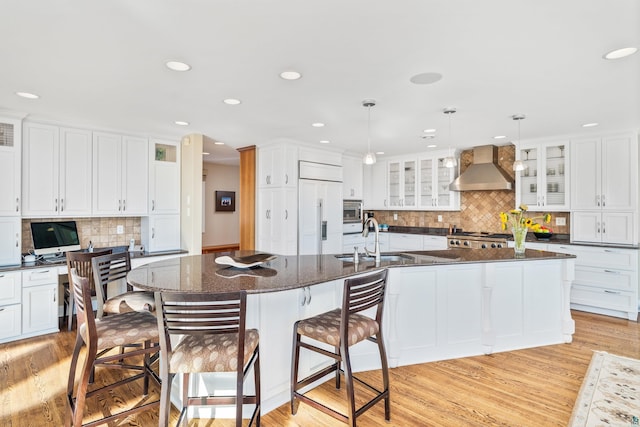 kitchen featuring wall chimney exhaust hood, light wood-style flooring, a sink, and built in appliances