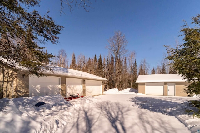 snow covered property with a garage and an outdoor structure