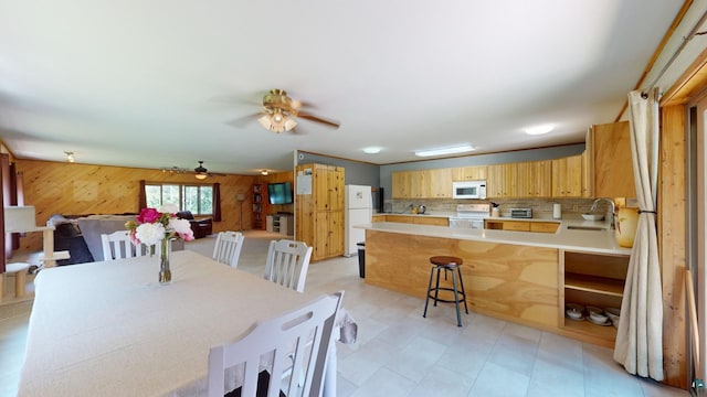 dining space featuring wooden walls, a ceiling fan, and light floors