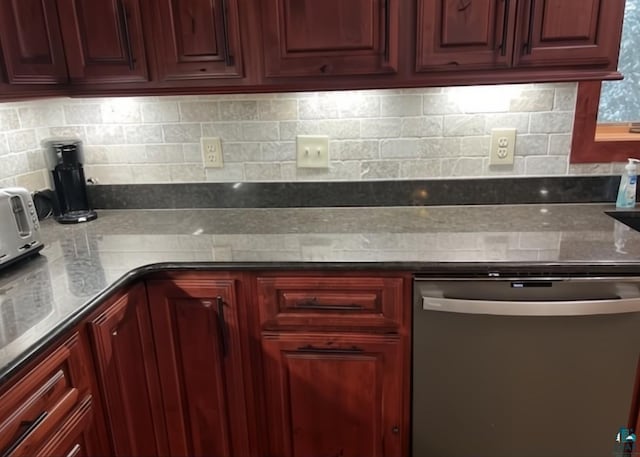 kitchen featuring reddish brown cabinets, stainless steel dishwasher, stone countertops, and decorative backsplash