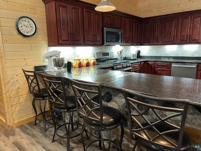 kitchen with stainless steel appliances, tasteful backsplash, dark countertops, wooden walls, and wood finished floors