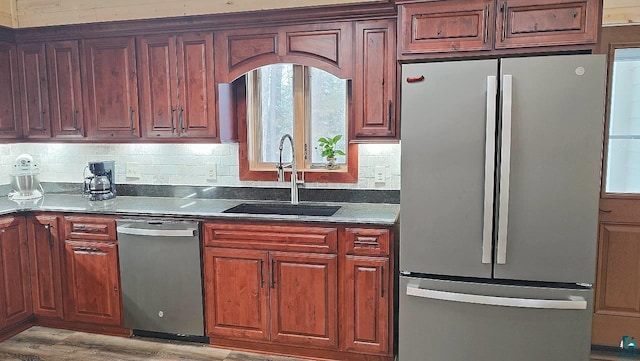 kitchen with stainless steel appliances, dark countertops, a sink, and backsplash