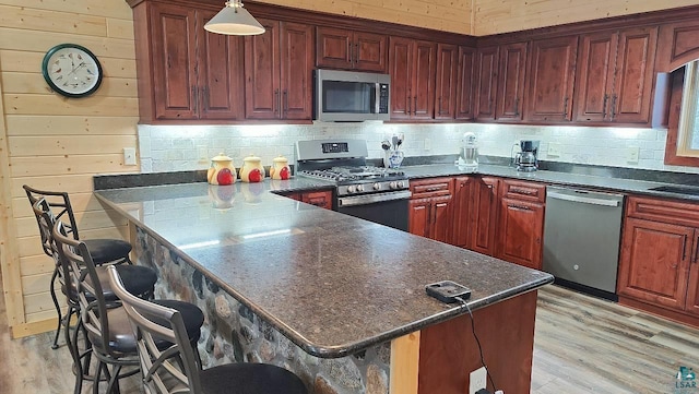 kitchen featuring tasteful backsplash, a kitchen breakfast bar, a peninsula, stainless steel appliances, and light wood-type flooring