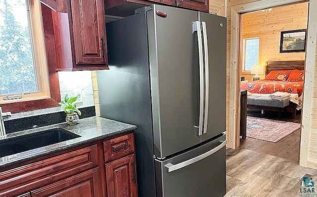 kitchen featuring light wood-style flooring, wooden walls, a sink, freestanding refrigerator, and dark stone countertops