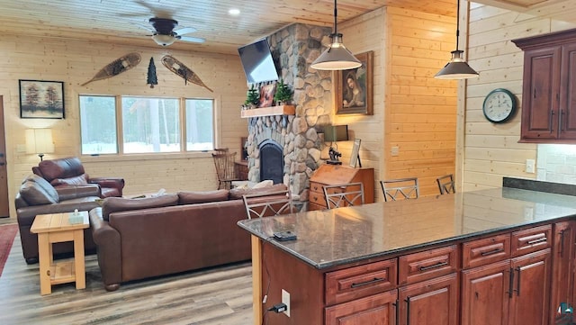 living area with light wood-style flooring, wood walls, a fireplace, wood ceiling, and a ceiling fan