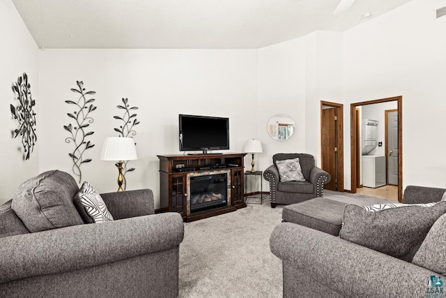 living area featuring visible vents, a glass covered fireplace, stacked washer / drying machine, and light colored carpet