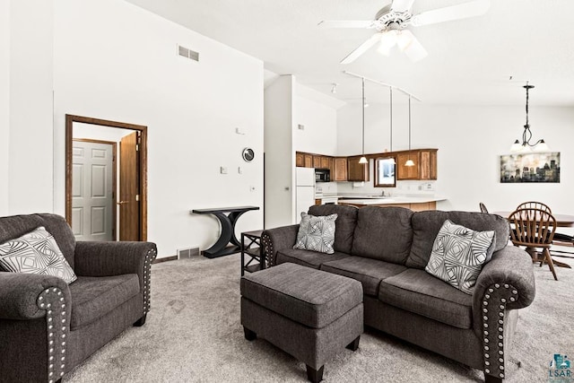 living area featuring light colored carpet, visible vents, a ceiling fan, high vaulted ceiling, and baseboards