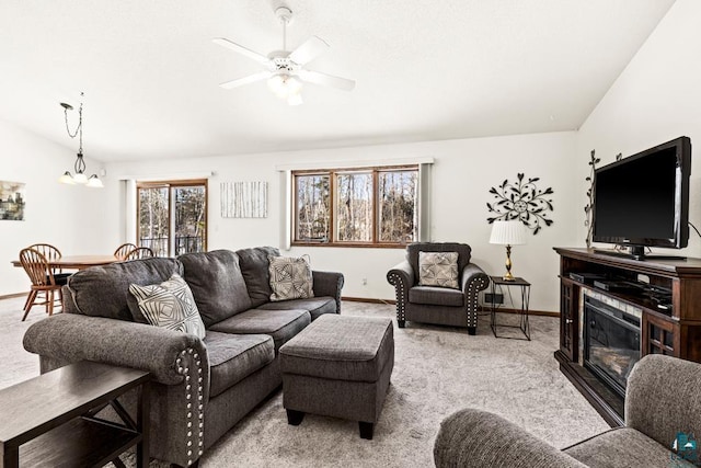 living room featuring lofted ceiling, ceiling fan with notable chandelier, carpet flooring, and a glass covered fireplace