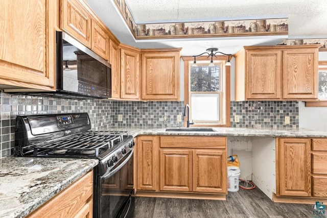 kitchen with light stone counters, a sink, backsplash, dark wood-style floors, and gas range oven