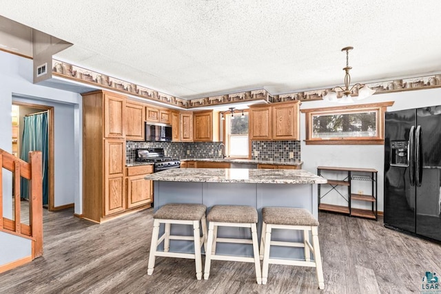 kitchen featuring decorative backsplash, a kitchen island, a breakfast bar area, appliances with stainless steel finishes, and wood finished floors