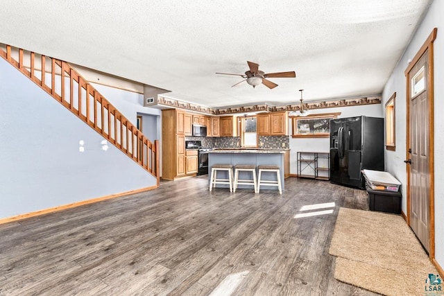 kitchen featuring dark wood-style floors, gas range oven, stainless steel microwave, backsplash, and black fridge